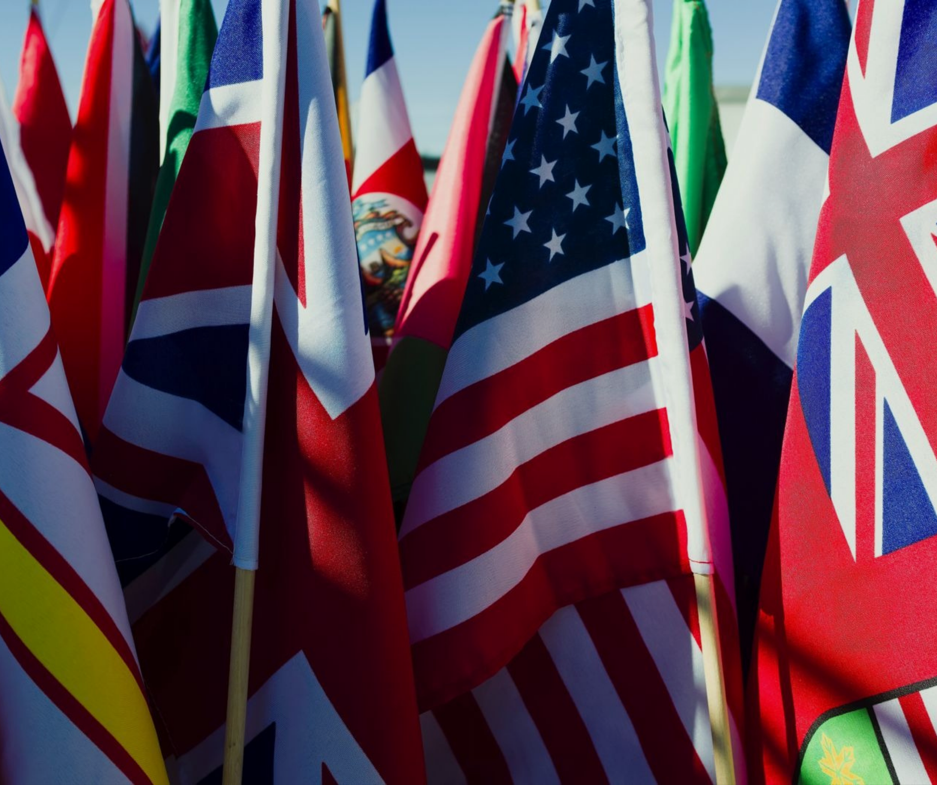 Un primo piano di diverse bandiere nazionali sovrapposte, tra cui la Union Jack e la bandiera a stelle e strisce degli Stati Uniti.