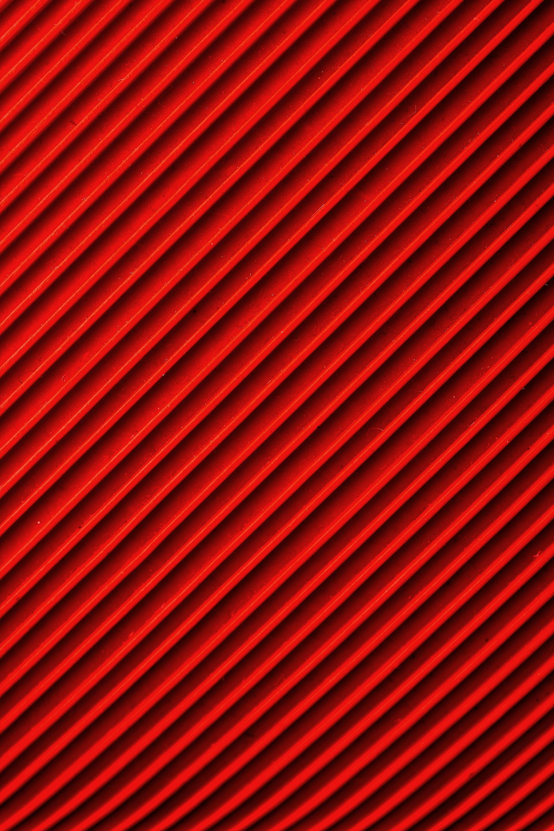 Sfondo rosso brillante caratterizzato da un motivo ripetuto di creste o scanalature diagonali equidistanti.