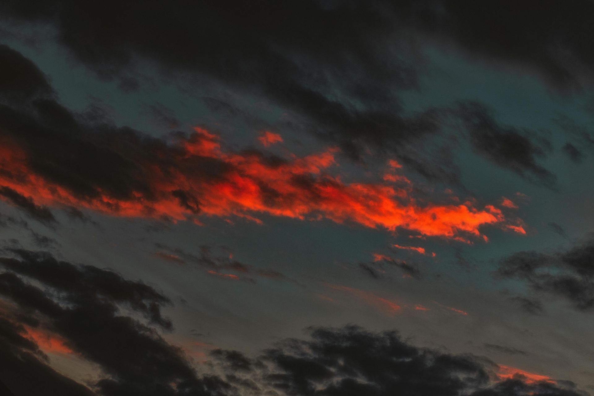 Una nuvola rosso fuoco e vibrante risplende sullo sfondo di un cielo serale blu intenso e cupo.