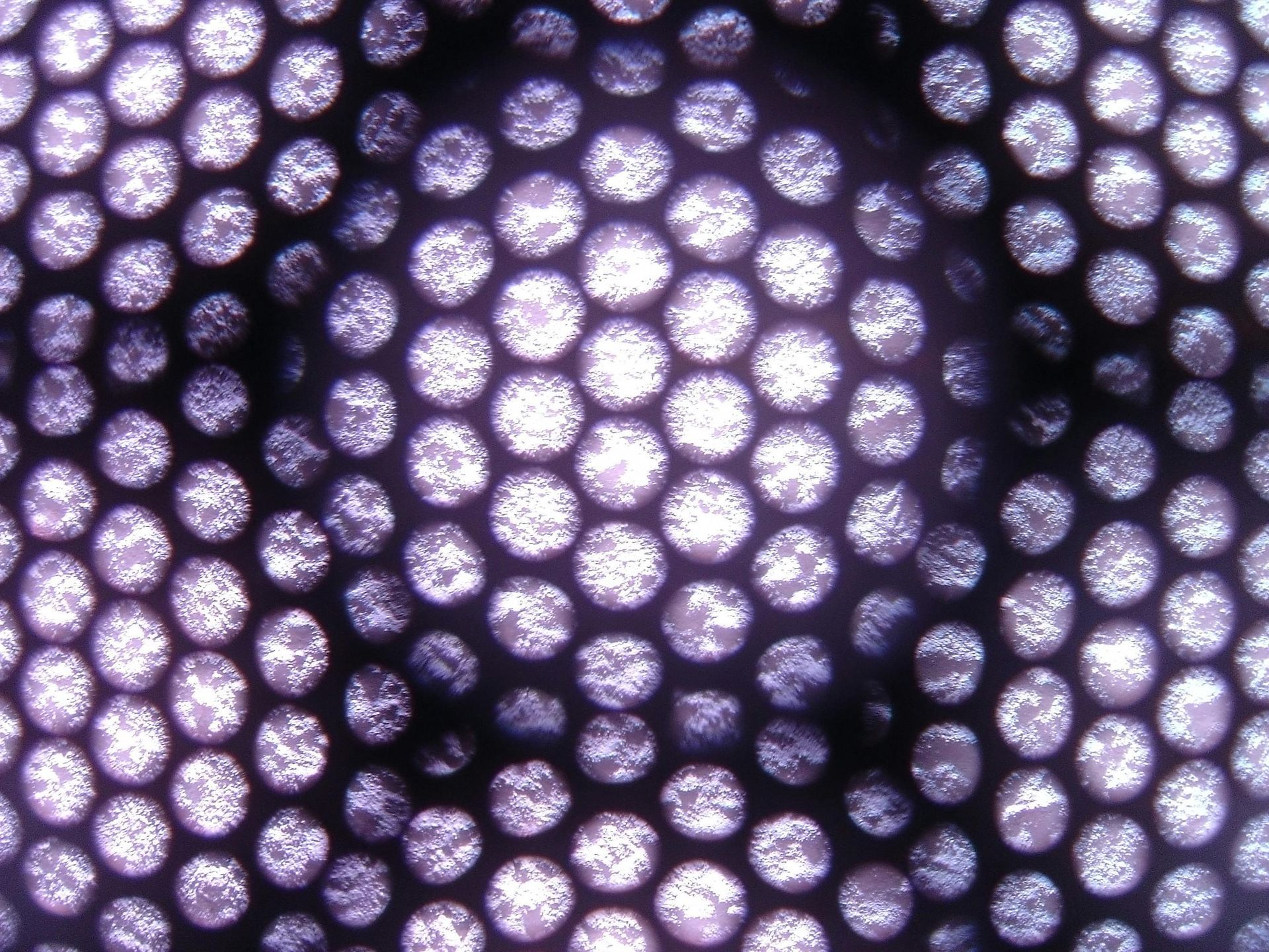 Vista ravvicinata di una griglia circolare scura e perforata con aperture circolari luminose e brillanti.