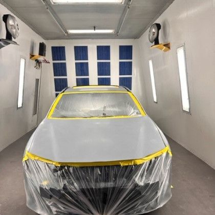 A car is covered in plastic in a paint booth.