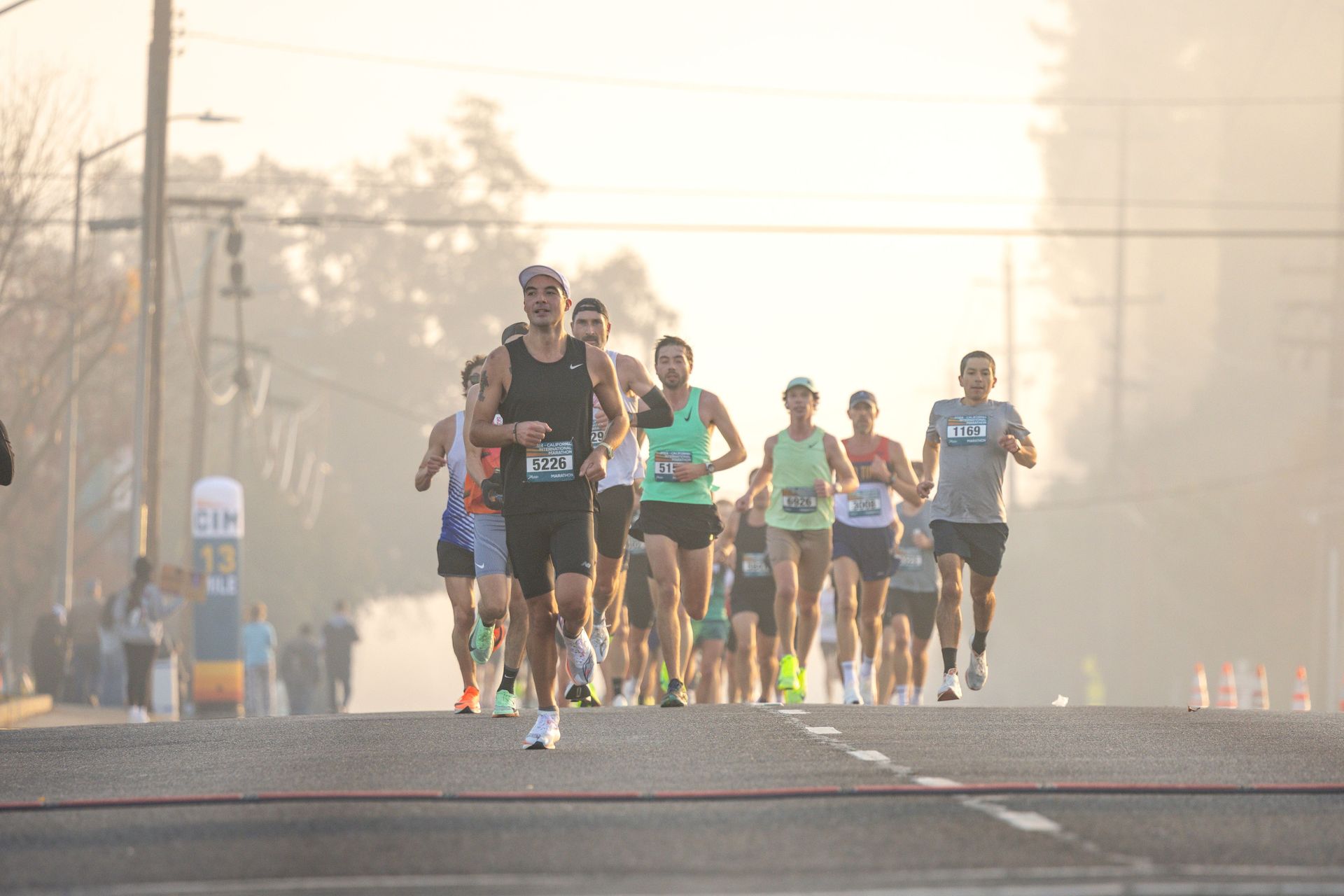 Runners competing in a road race at sunrise on a hazy city street