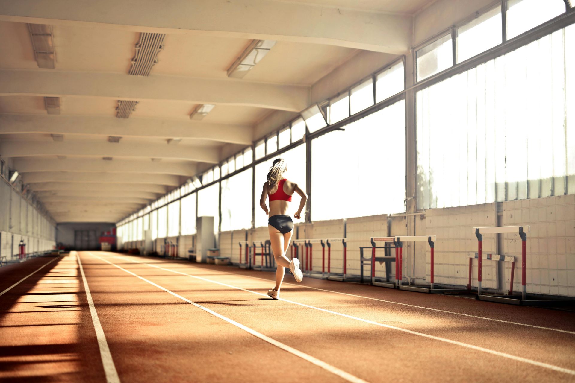Runner on an indoor track, running toward the camera in a sunlit training hall.
