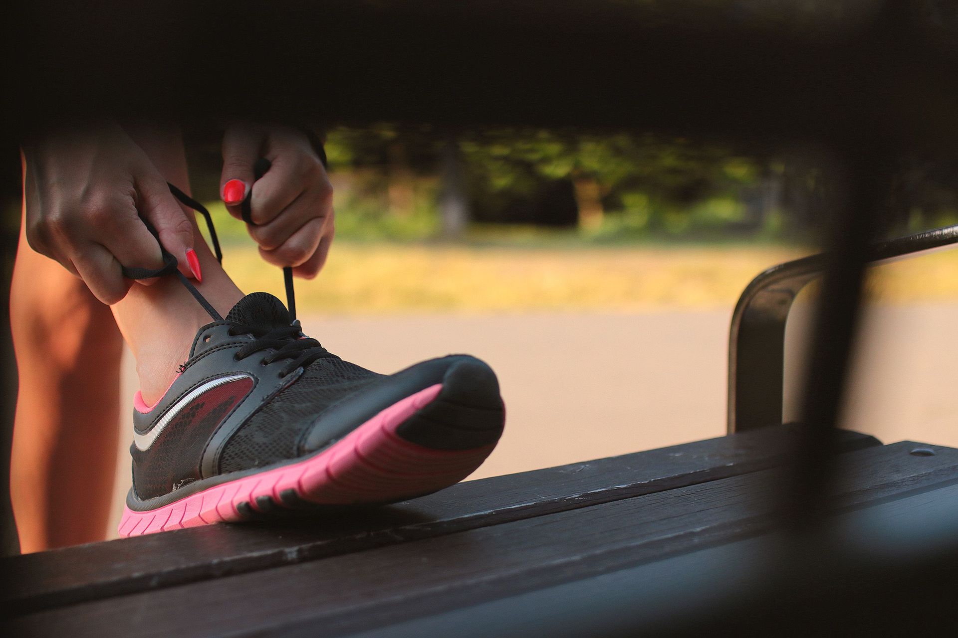 Hands tying a black and pink running shoe on a treadmill