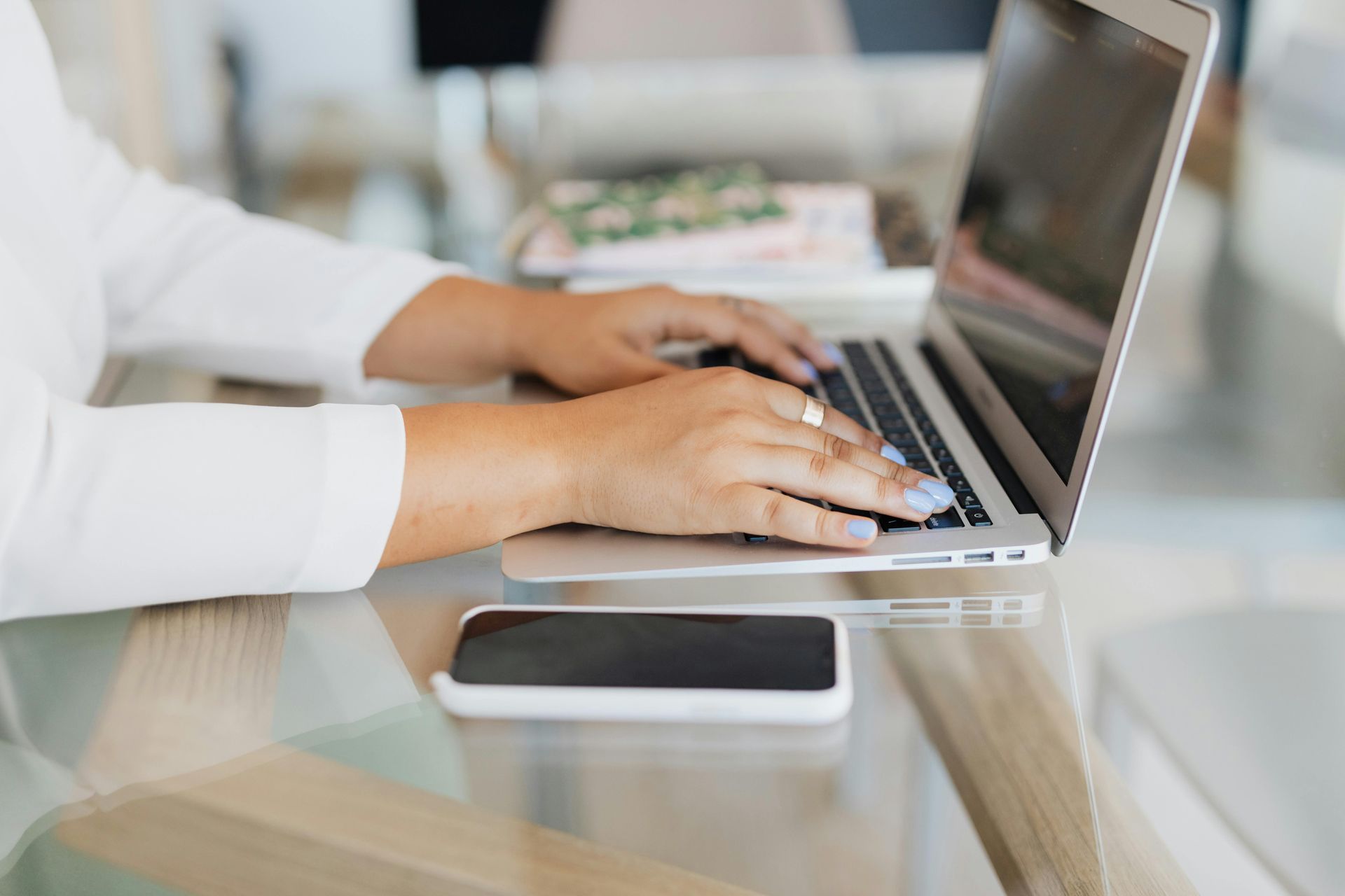 Hands using a laptop beside a bowl of colorful fruit on a white desk