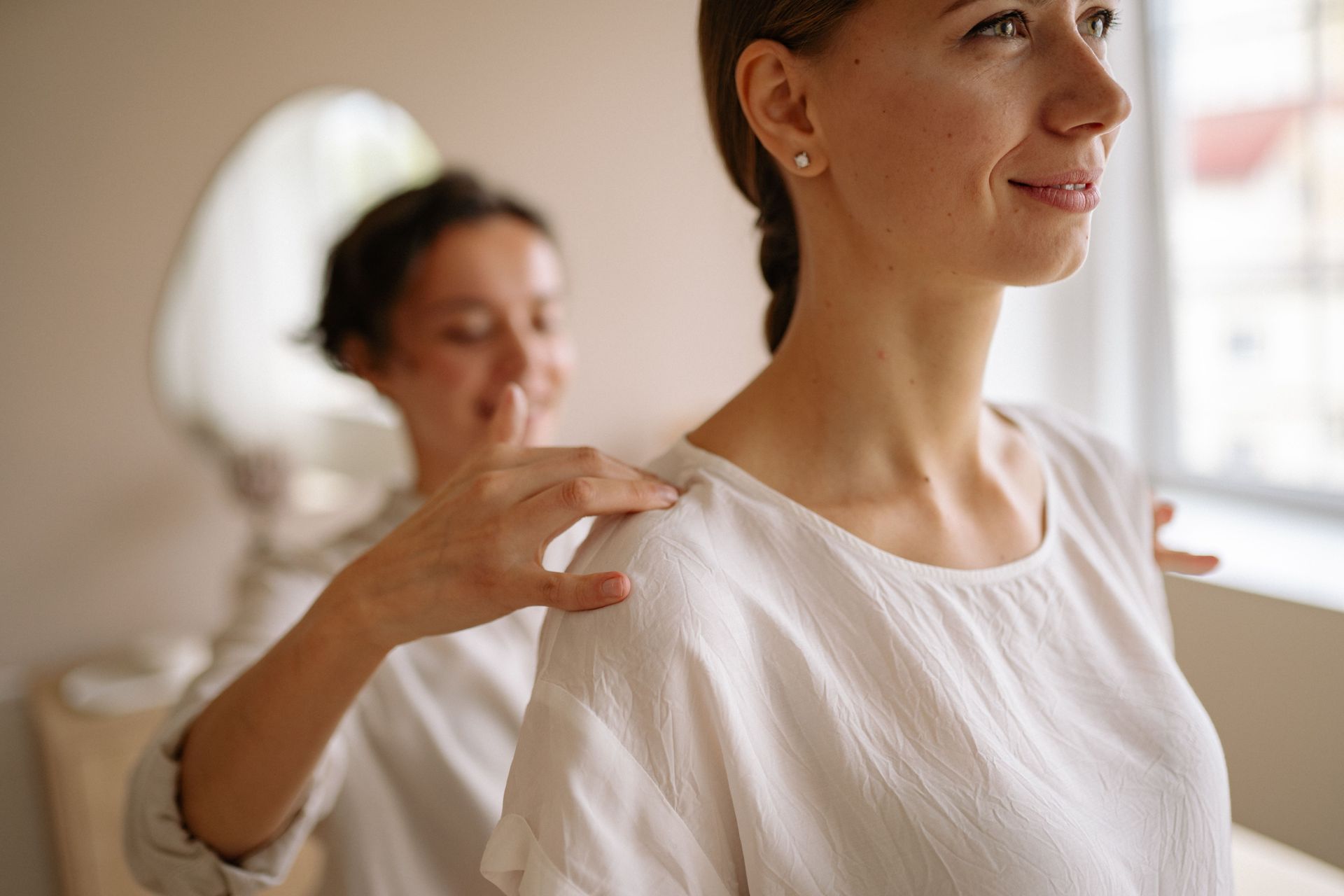 Woman receiving a shoulder massage in a bright room, with another person in the background