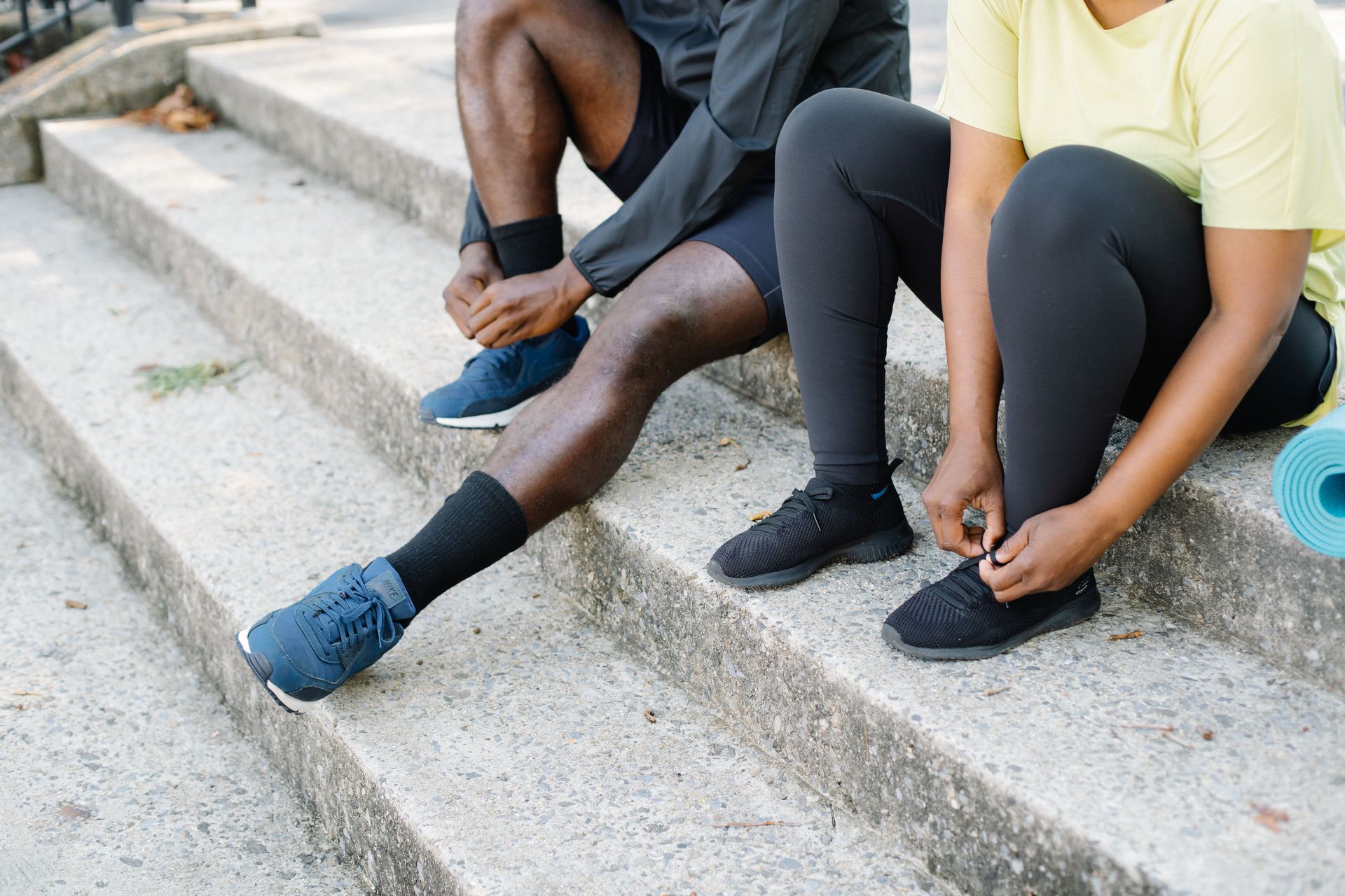 Two people sitting on concrete steps, tying their shoelaces before exercise