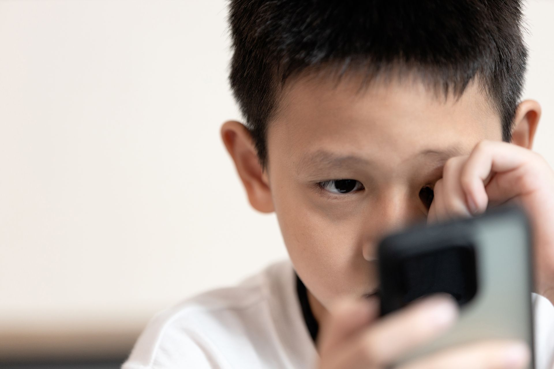 Child looking at a smartphone with a focused expression, close-up indoors