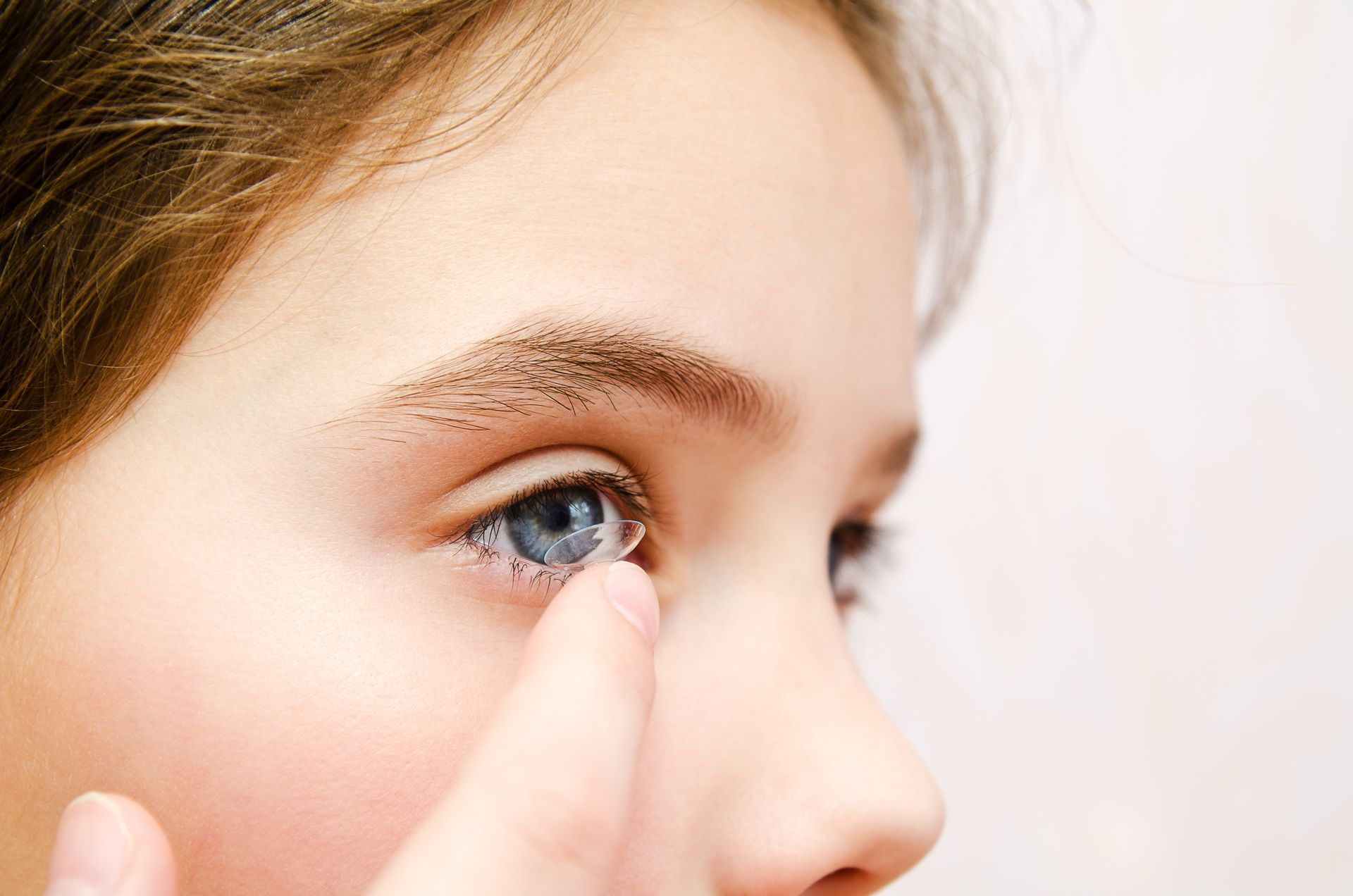 Close-up of a child gently touching an eye while looking sideways