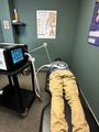 Person lying face down on a treatment table in a small clinic room with medical equipment nearby