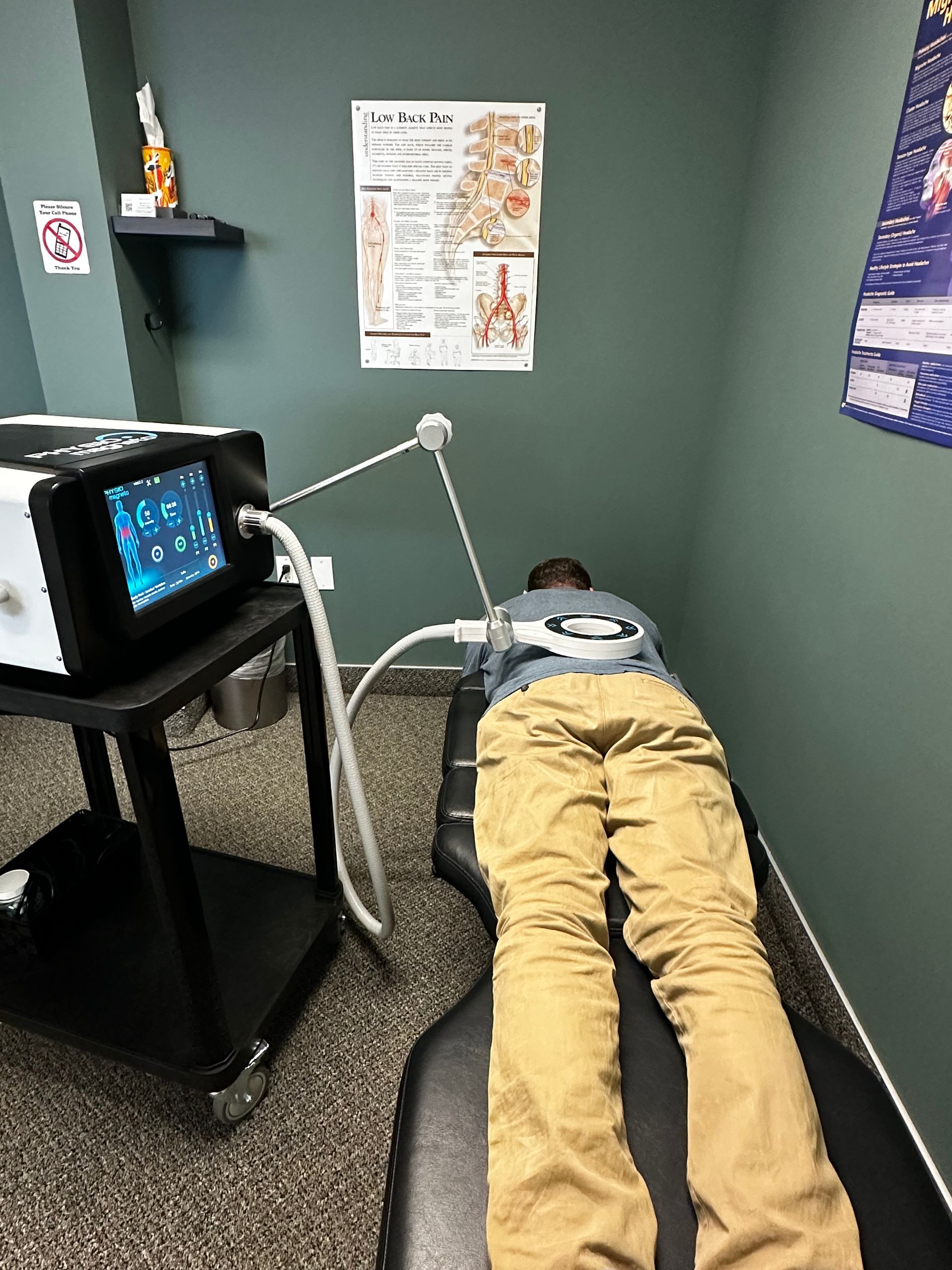 Person lying on a padded exam table in a small therapy room receiving PEMF therapy.