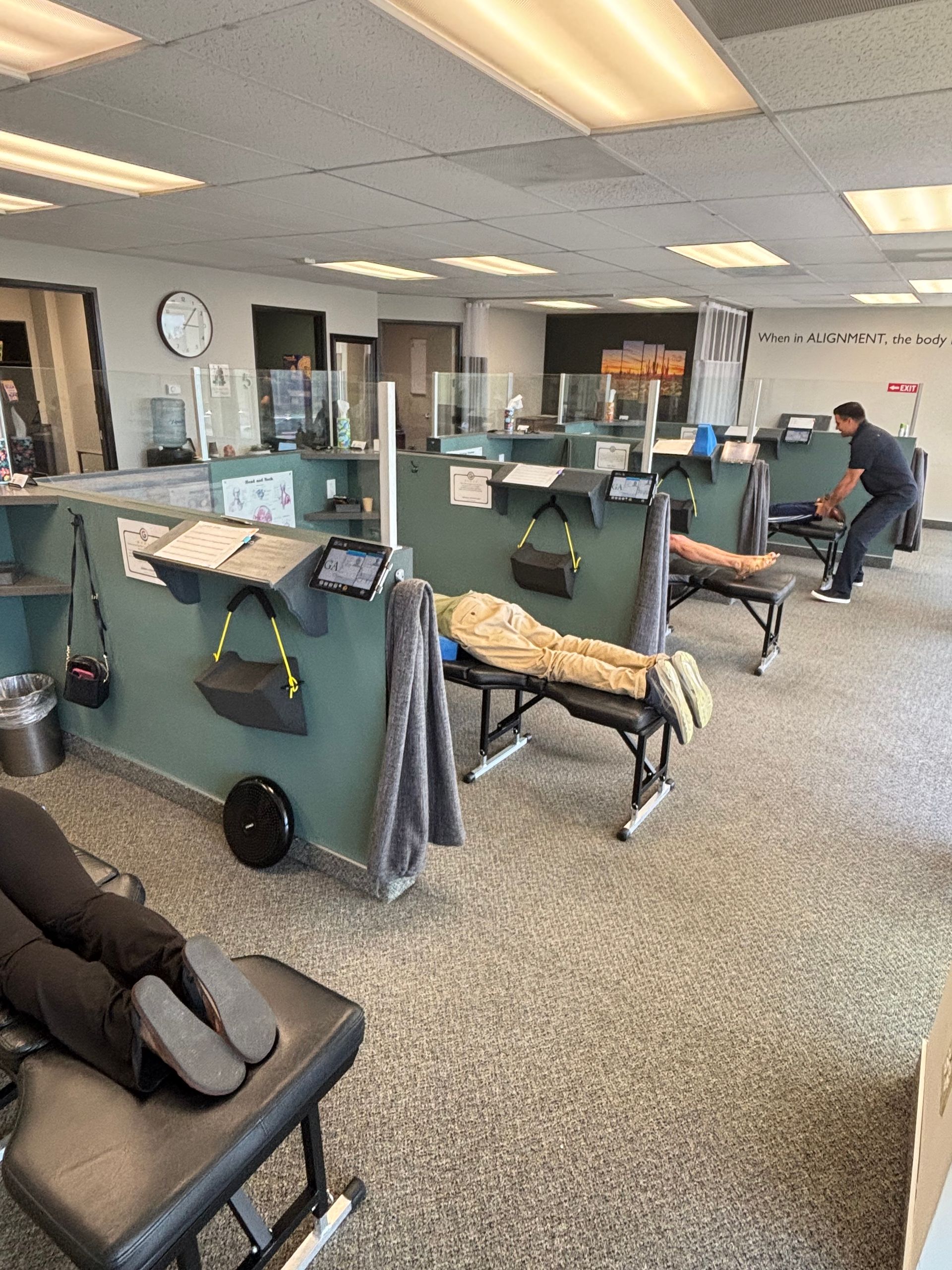 Office with spaced desks, chairs, and partition screens; one person sits at a desk in the background.