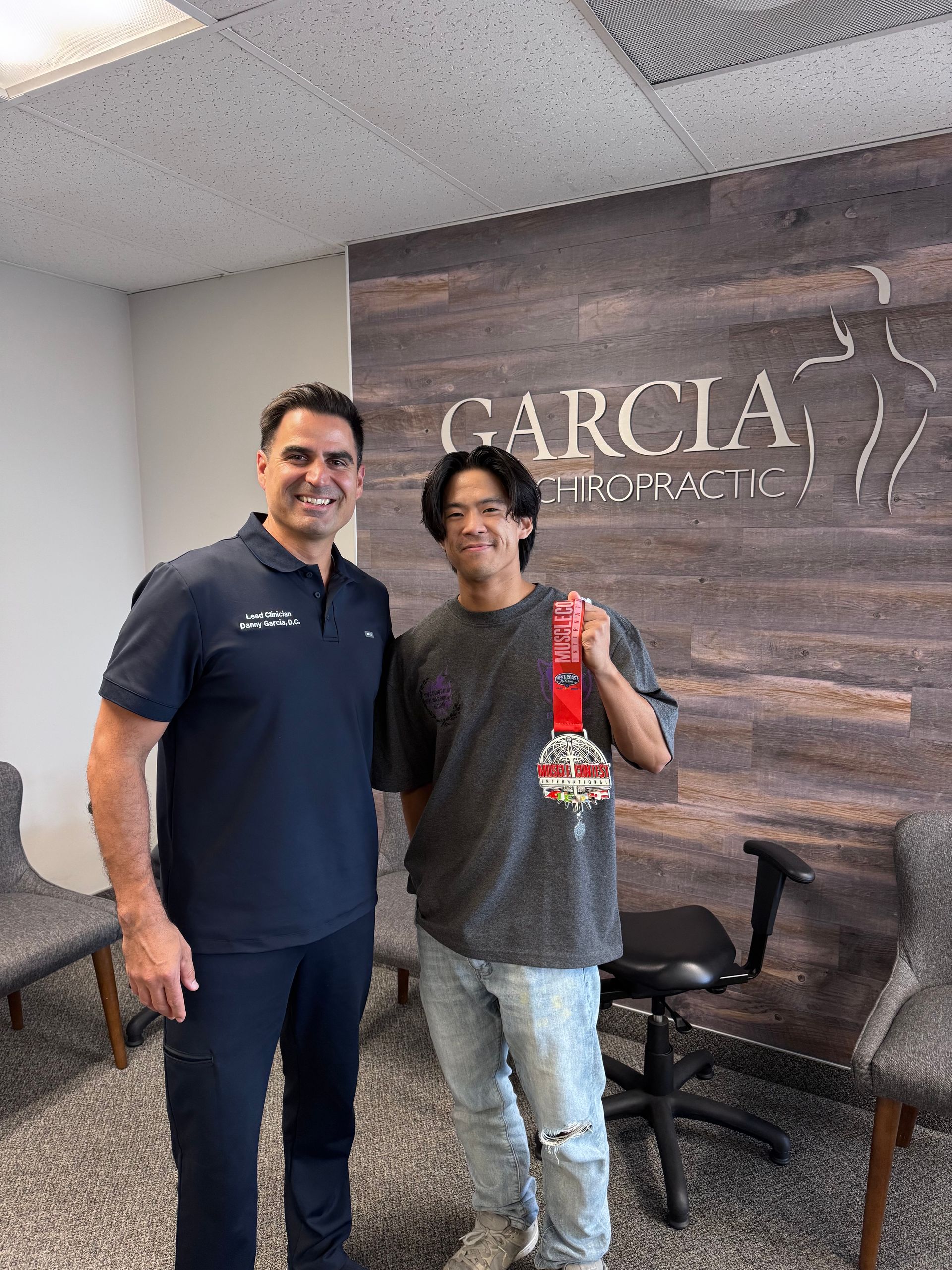 Two people standing in an office lobby, smiling and holding a red packaged item in front of a Garcia sign