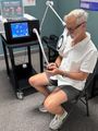 Person seated beside a PEMF therapy device, using a controller in a clinic setting