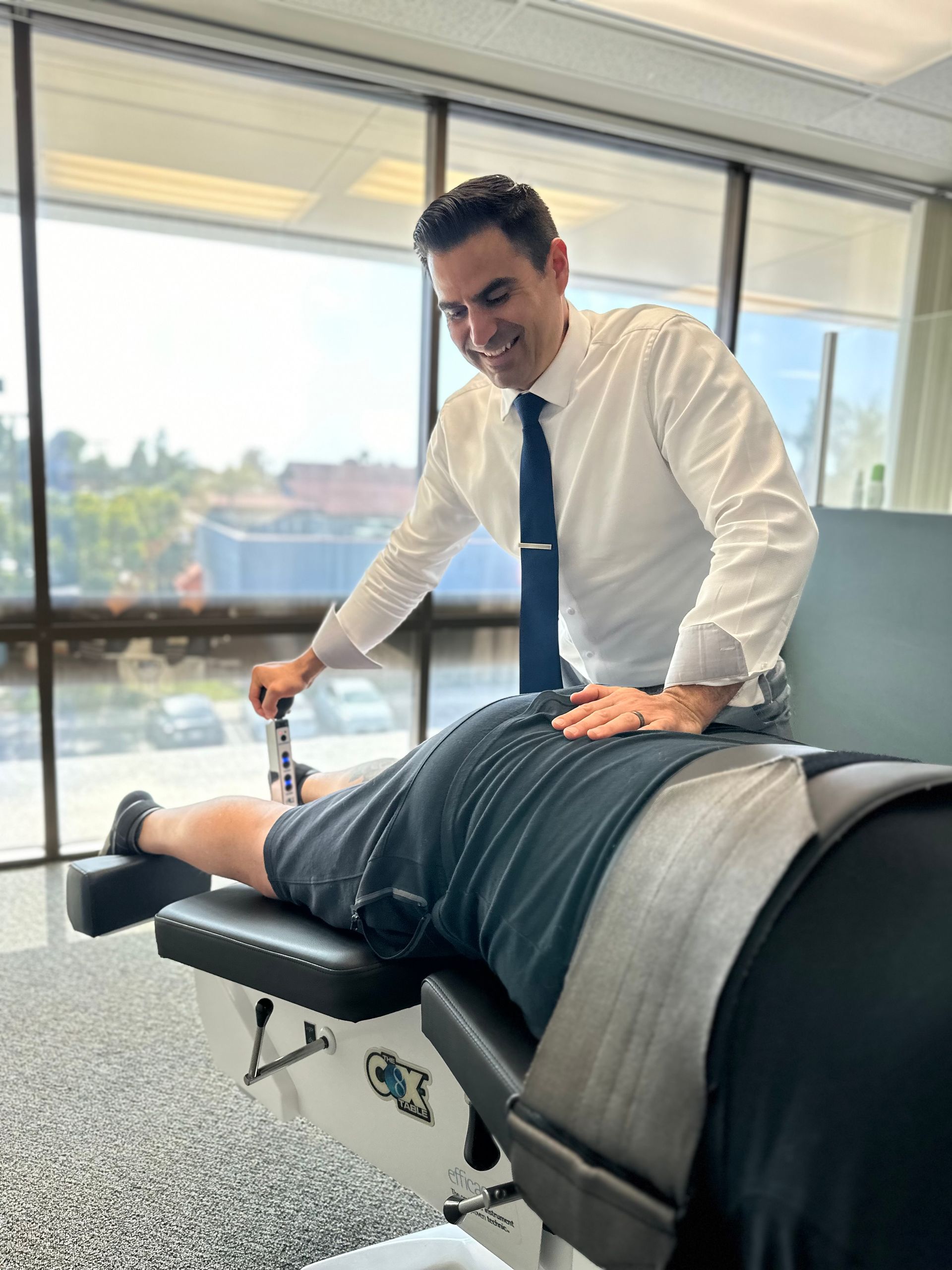 Chiropractor adjusting a patient on a treatment table in a bright office overlooking water