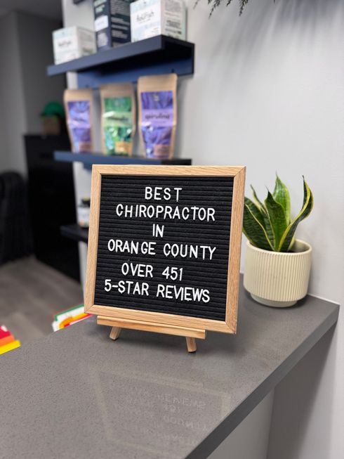Desk sign reading “Best Chiropractor in Orange County over 45 5-star reviews” beside a potted plant.