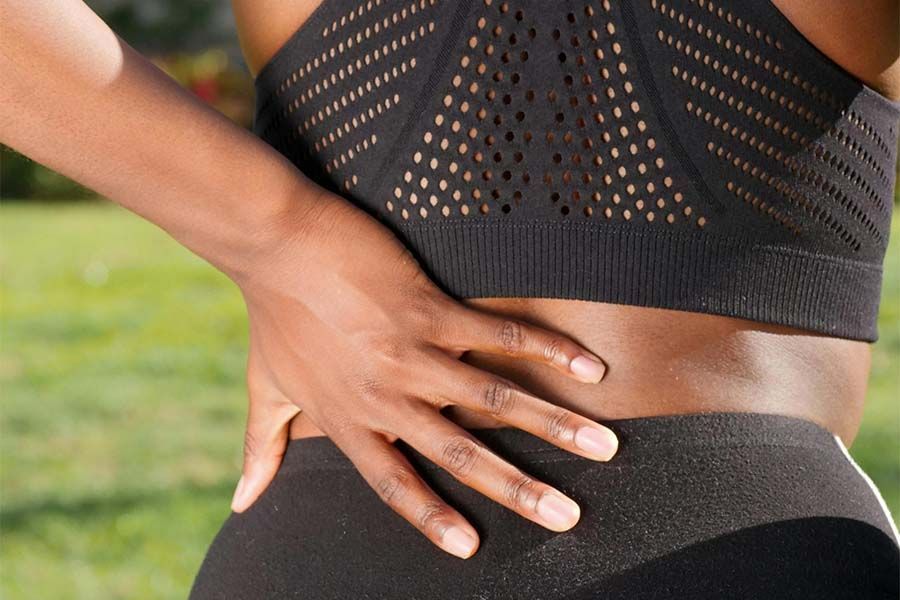 Hand on lower back during exercise, wearing black athletic clothing outdoors.