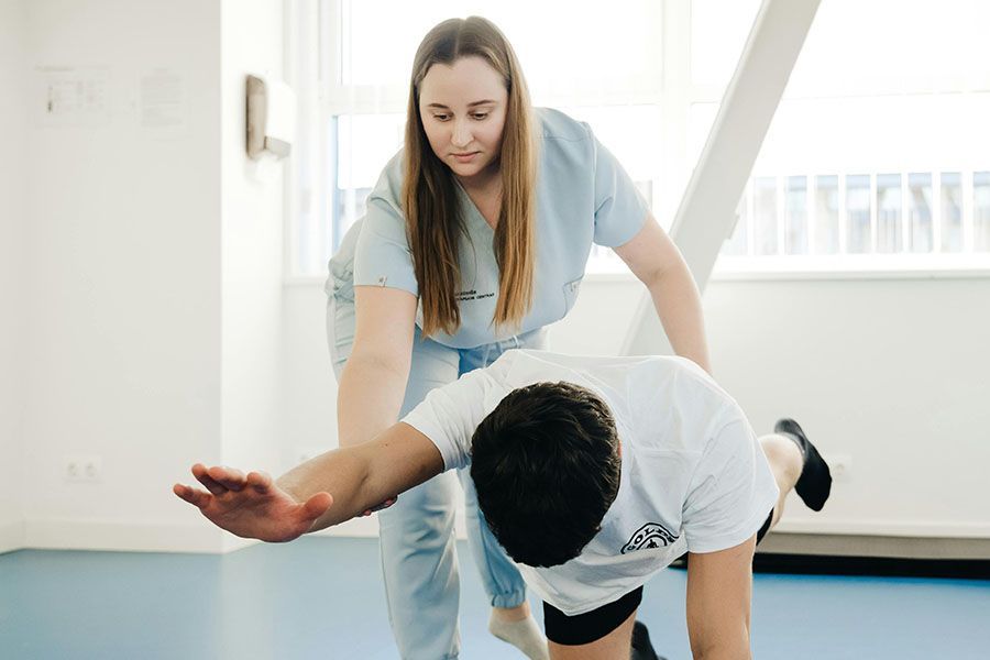 Physical therapist assisting a bent-over patient during a rehabilitation exercise in a bright room