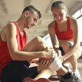 Two athletes in red sportswear tending to a wrapped ankle on an indoor gym floor