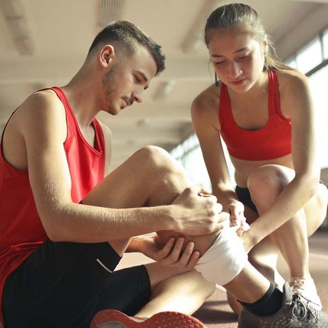 Two athletes in red uniforms tying a bandage in a bright gymnasium