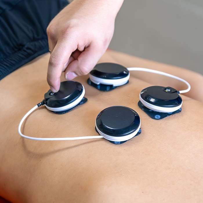 Hand placing black electrode pads on a person’s bare back during massage or therapy treatment