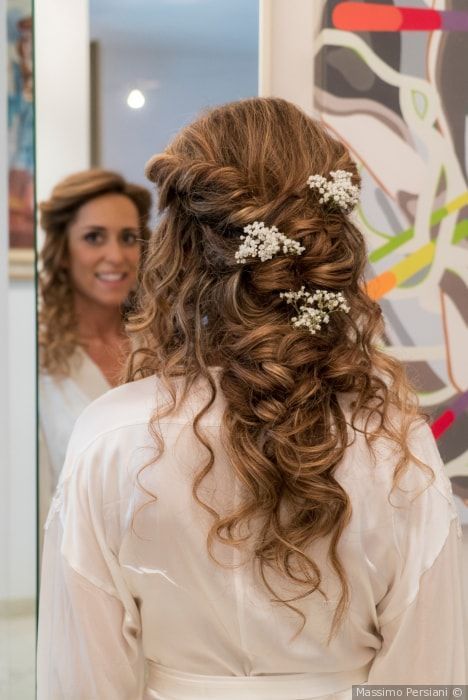 Donna con i capelli ricci raccolti e adornati con fiori bianchi, che si guarda allo specchio.