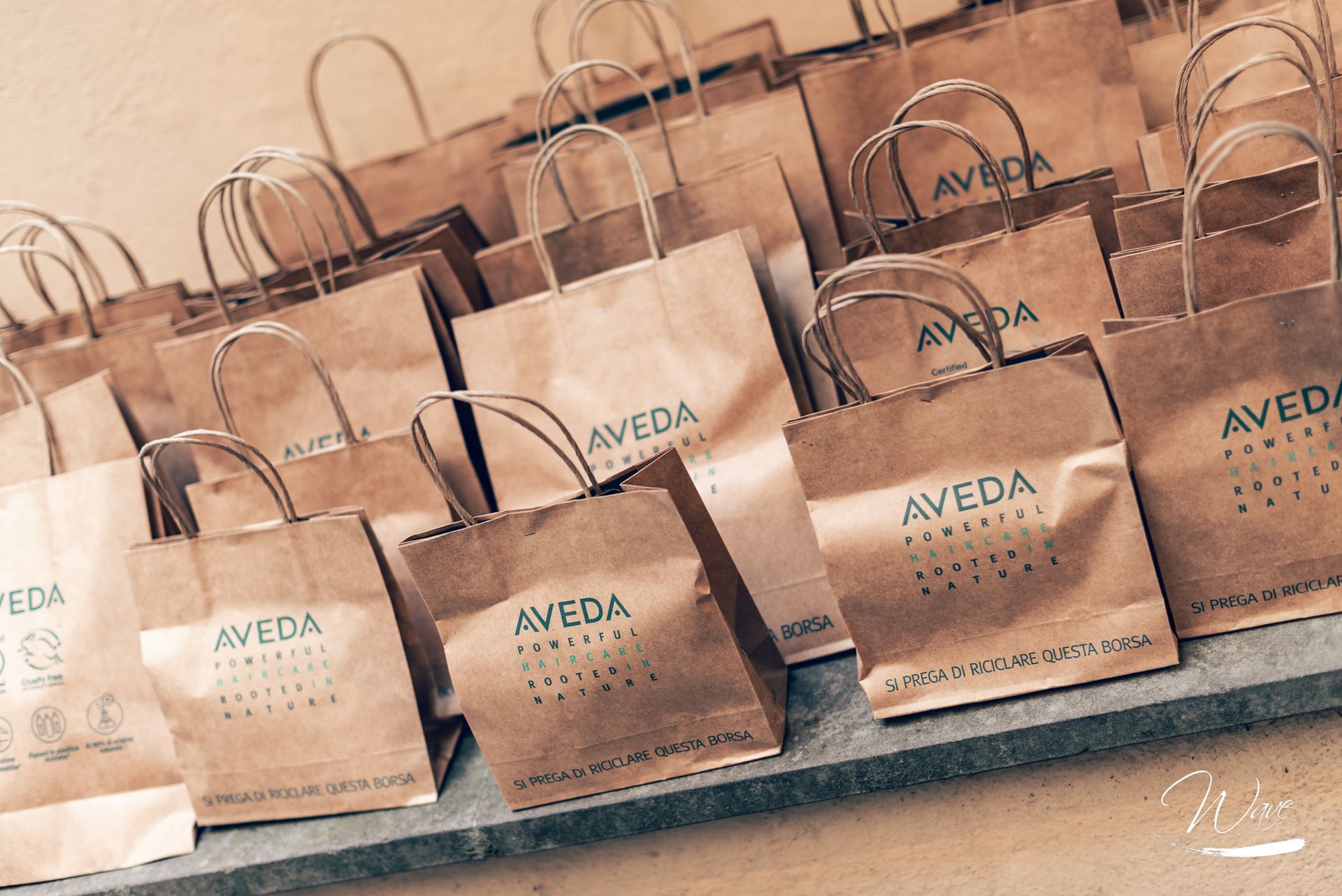 Borse della spesa in carta marrone Aveda disposte su uno scaffale, con il logo Aveda visibile.