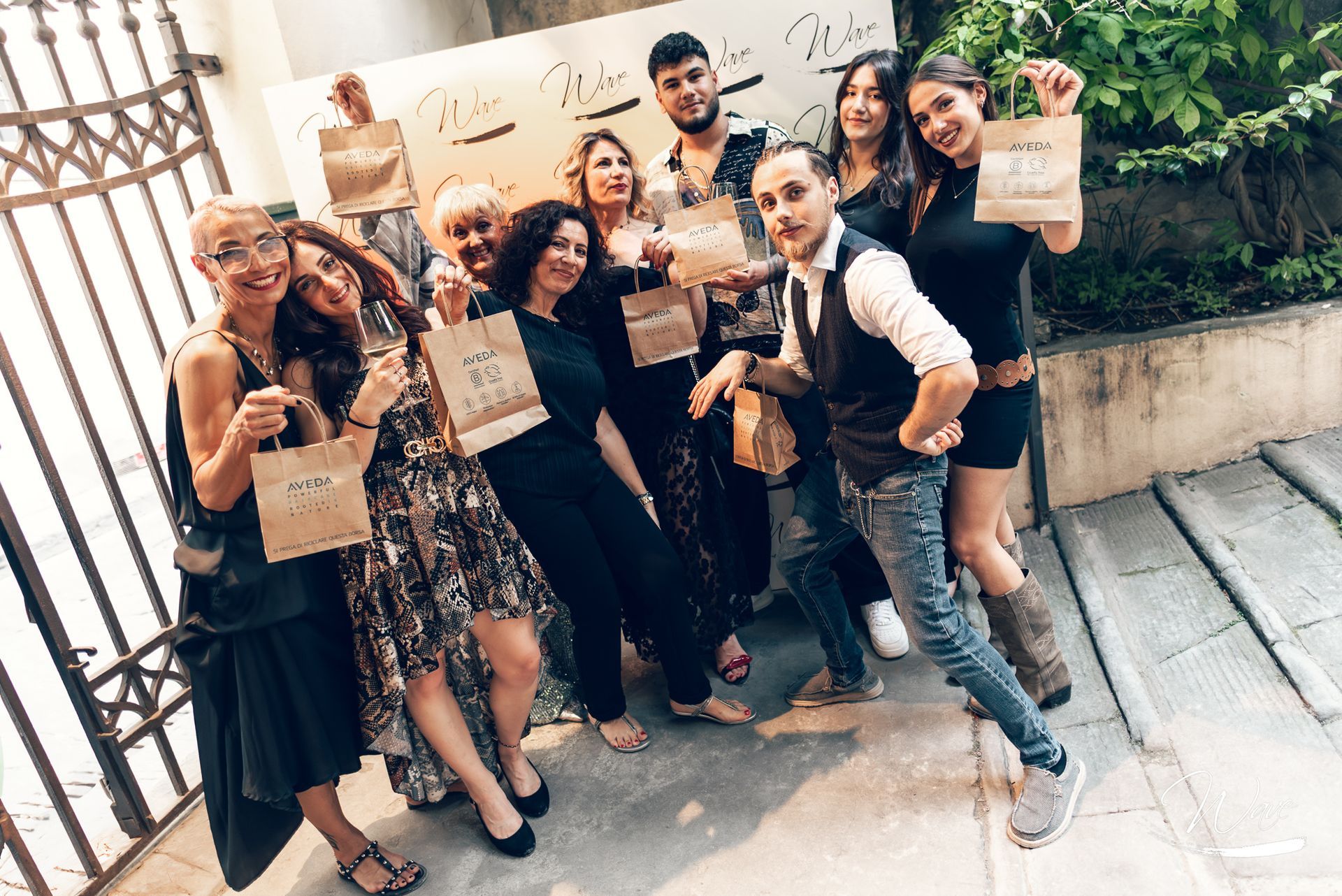 Gruppo di persone in posa con sacchetti regalo davanti a un cancello. All'aperto, sorrisi.