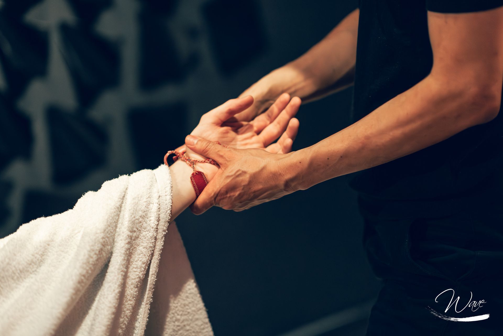 Persona che massaggia una mano avvolta in un asciugamano bianco, sfondo scuro.
