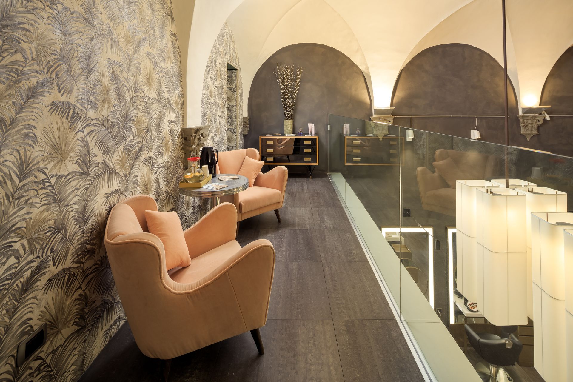 Two peach armchairs in a room with patterned wallpaper, a glass railing, and arched ceilings.