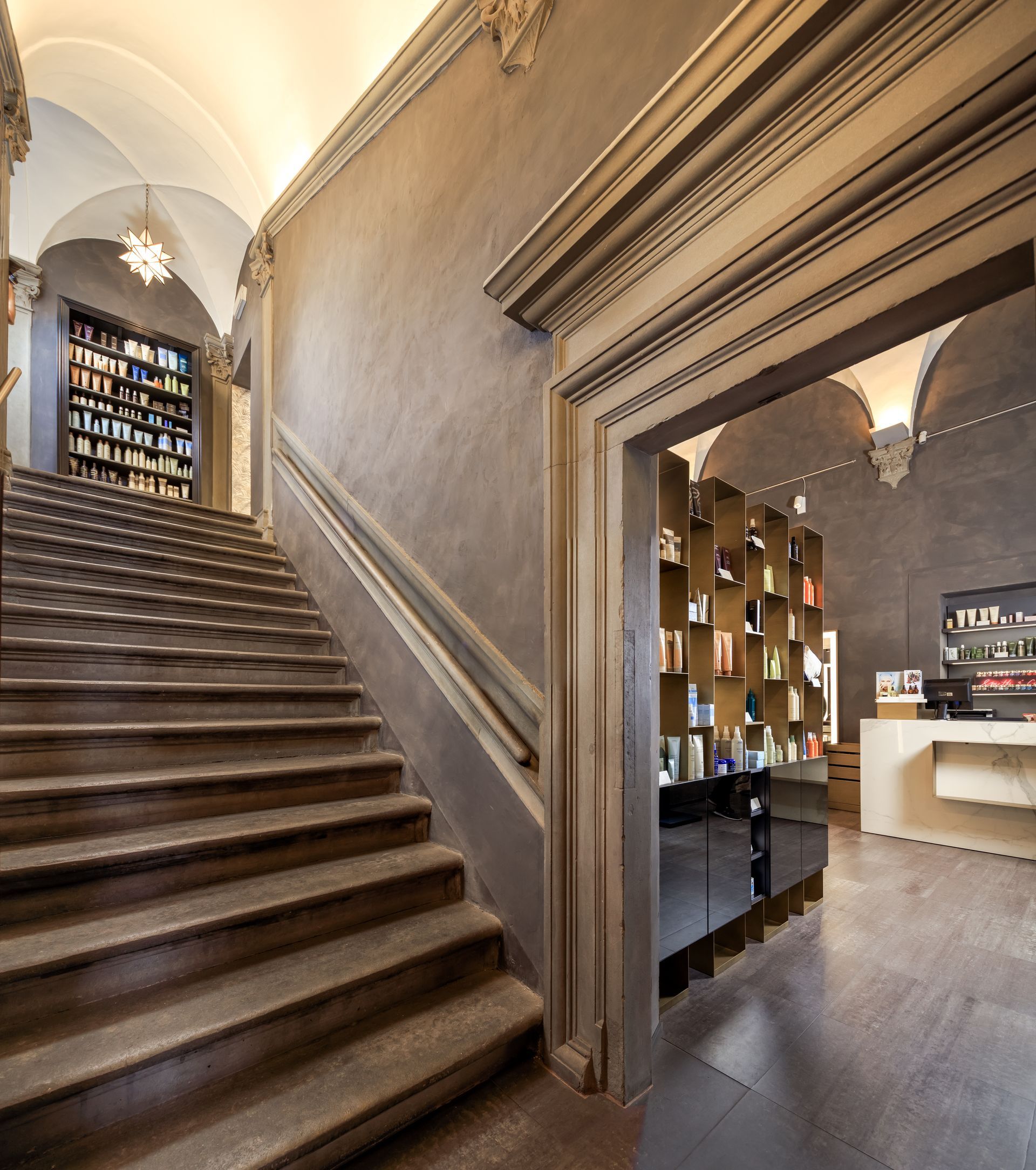 Stone staircase leading to a library, and an arched doorway to a shop interior. Grey walls, shelves of books.