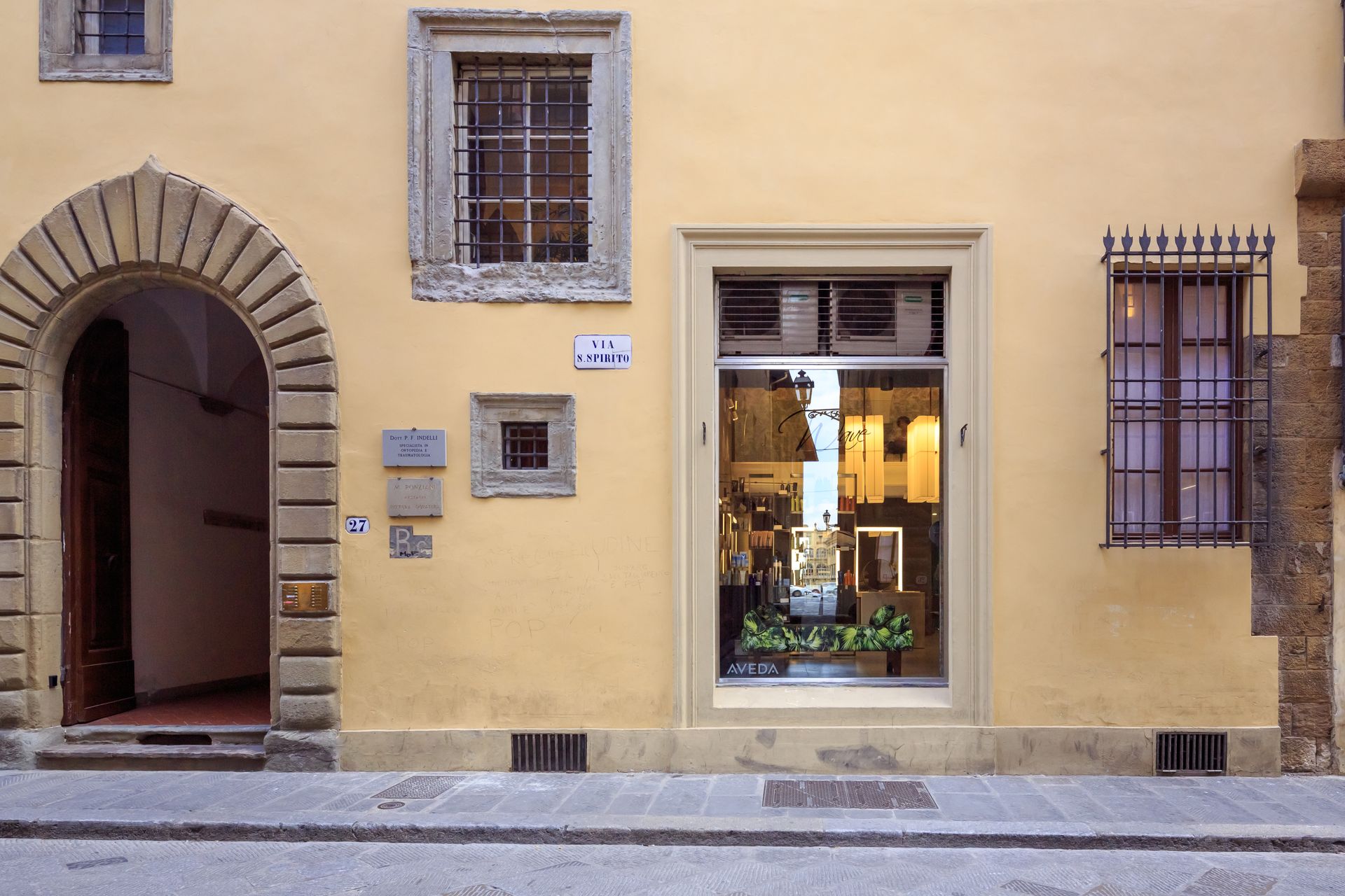 Building facade with arched doorway, shop window, and barred windows on a yellow wall.