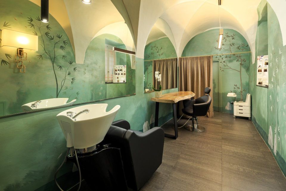 Hair salon interior with green walls, wash basin, chairs, large mirrors, and arched ceilings.
