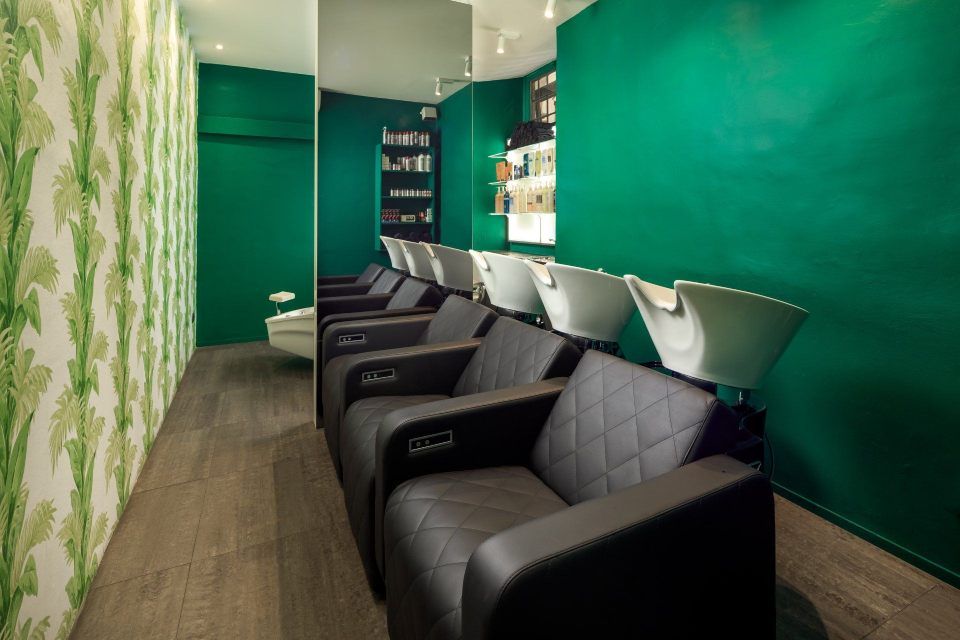 Hair salon with black chairs, wash basins, green walls, and floral wallpaper.