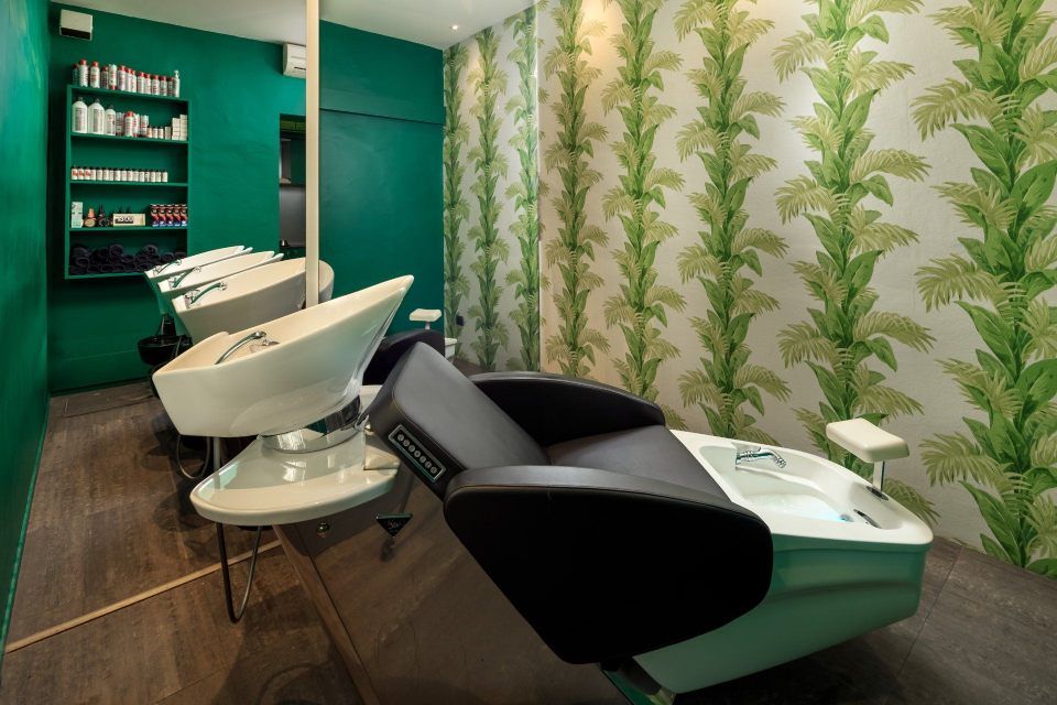 Salon interior with green accents, including wash stations, chairs, and patterned wallpaper.