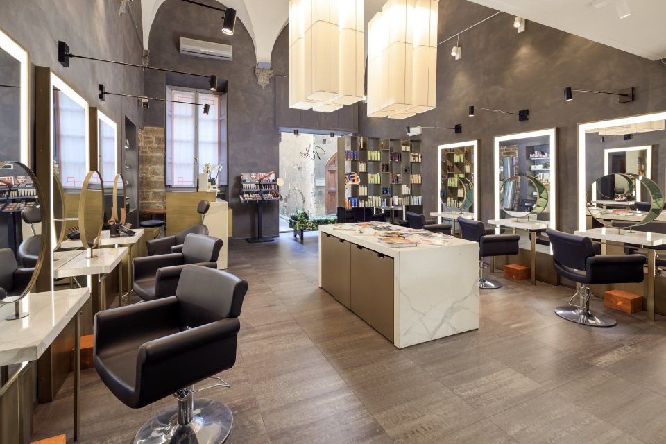 Hair salon interior with modern design, featuring styling stations, chairs, mirrors, and a central display.