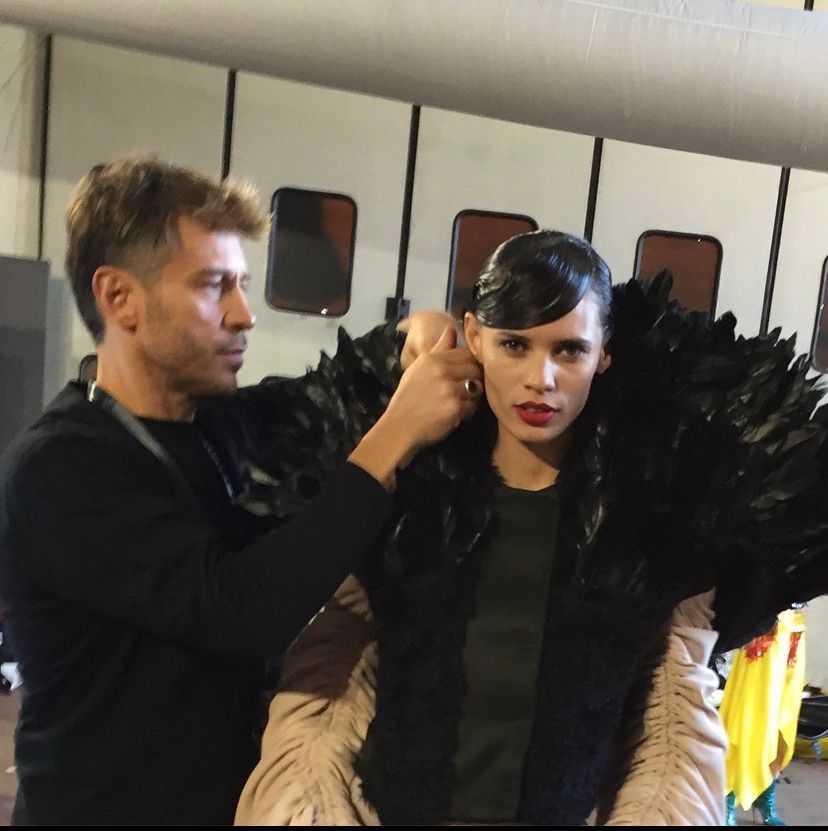 Uno stilista sistema il colletto di piume di una modella nel backstage. Top nero, pelle chiara.