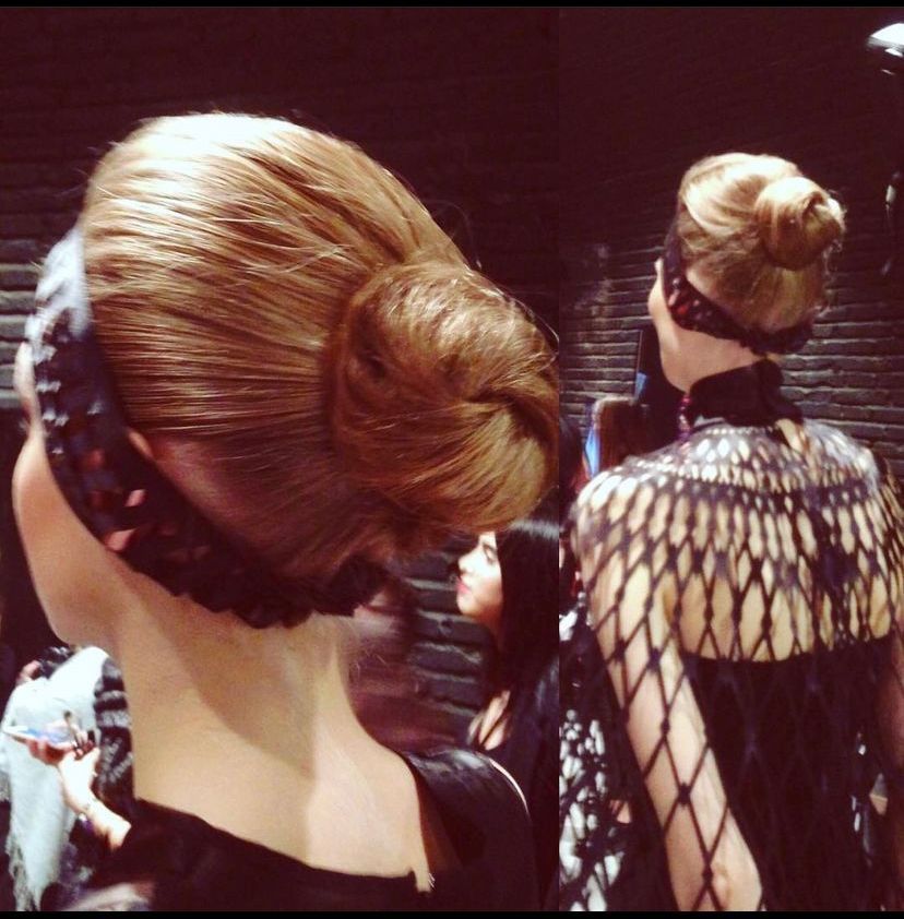 Due modelle con chignon alto e abiti scuri, nel backstage di una sfilata di moda.