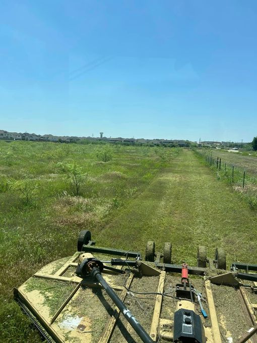 View from a tractor mowing a grassy field with a town in the distance under a blue sky.