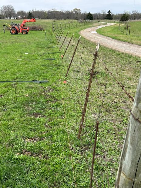 A fence being installed along a grassy field path, with an orange tractor in the distance.