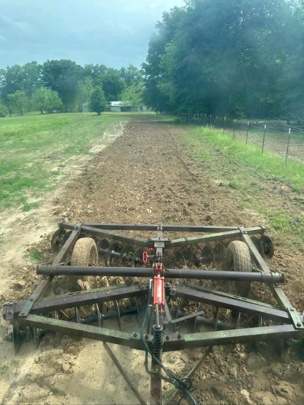A tractor harrowing a field of brown earth, trees and sky in the background.