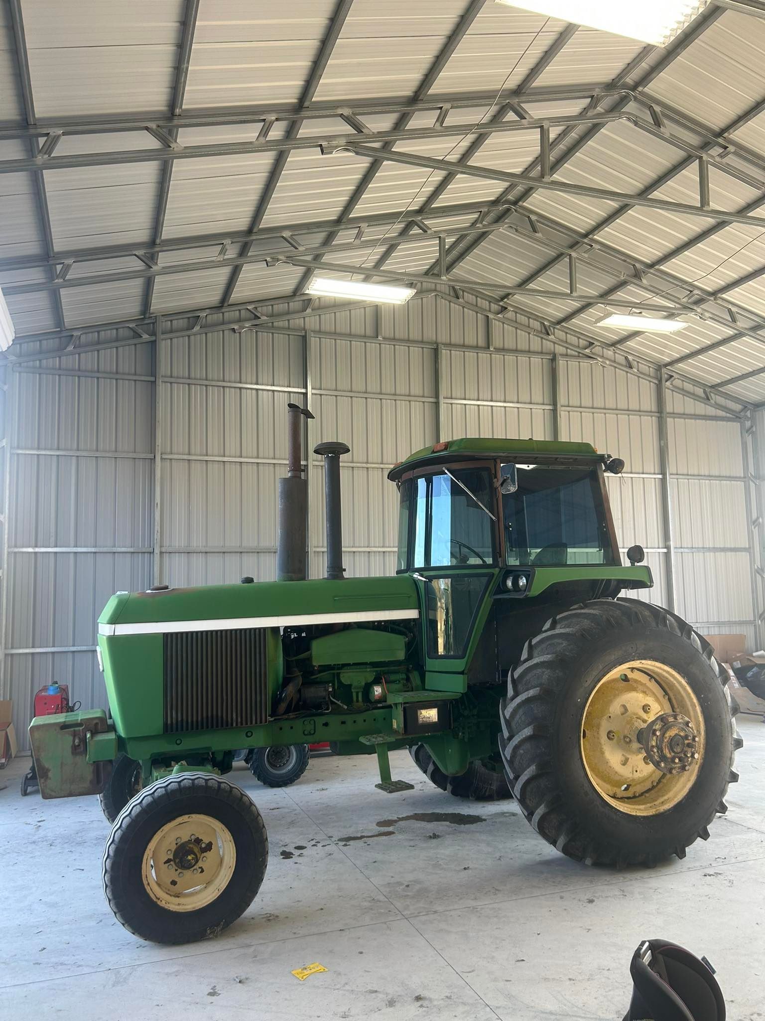 Green John Deere tractor parked inside a metal-walled building.