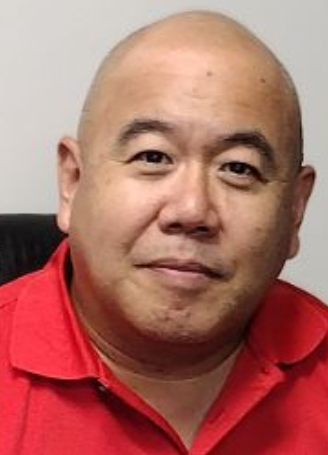 A bald man in a red shirt is smiling for the camera.