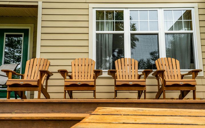 Four wooden rocking chairs lined up on a porch in front of a house window
