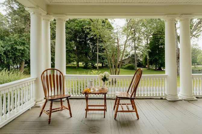 White porch with rocking chairs and a small table overlooking a green garden