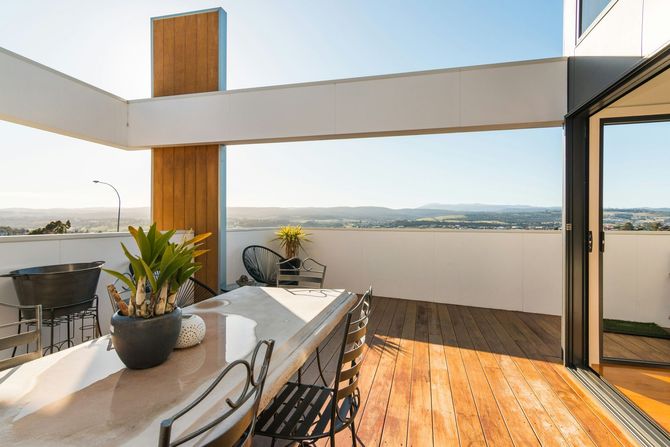 Modern patio with dining table, potted plants, wooden deck, and panoramic ocean view