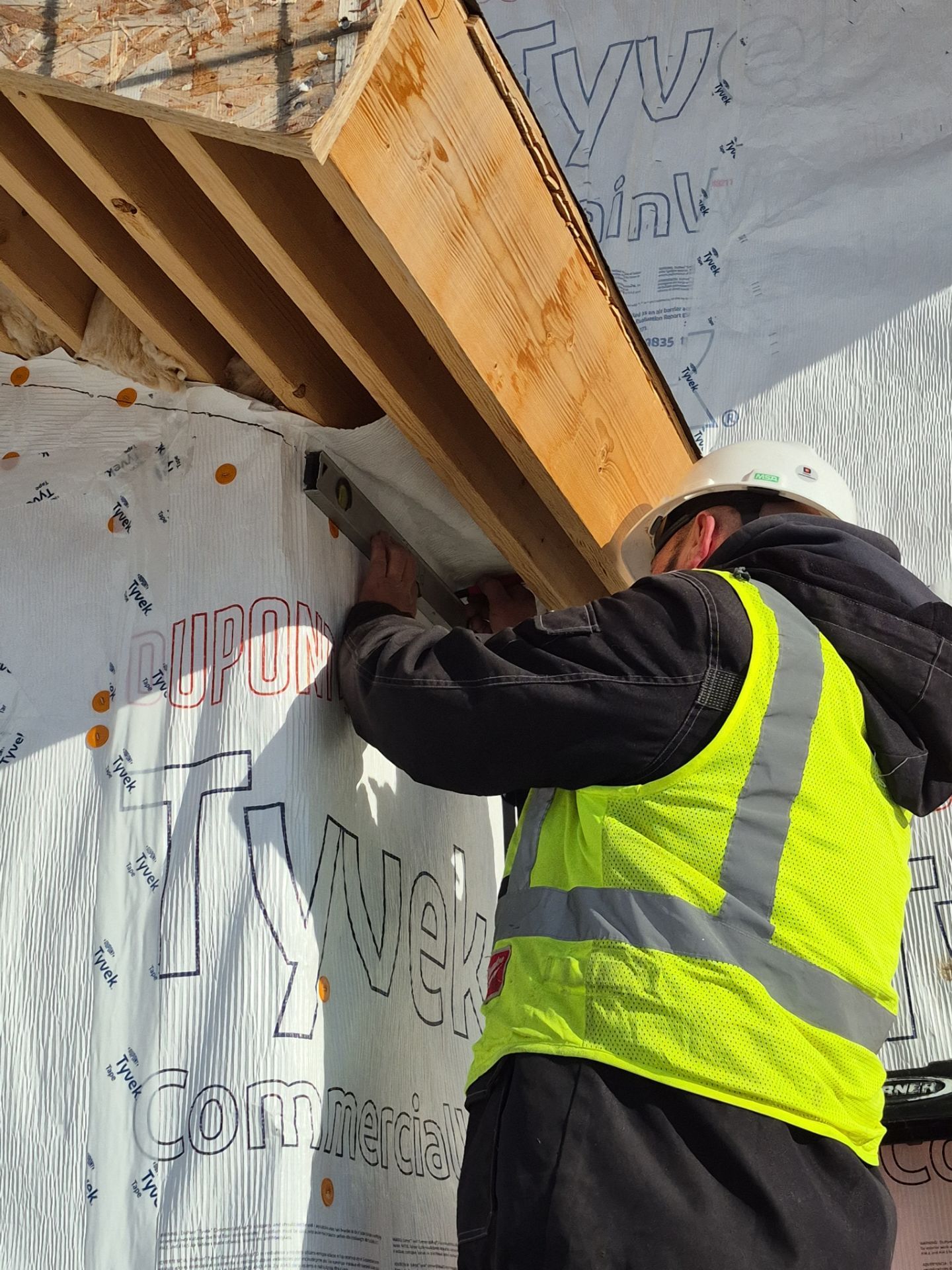 Worker in a yellow safety vest securing wood framing at a construction site.