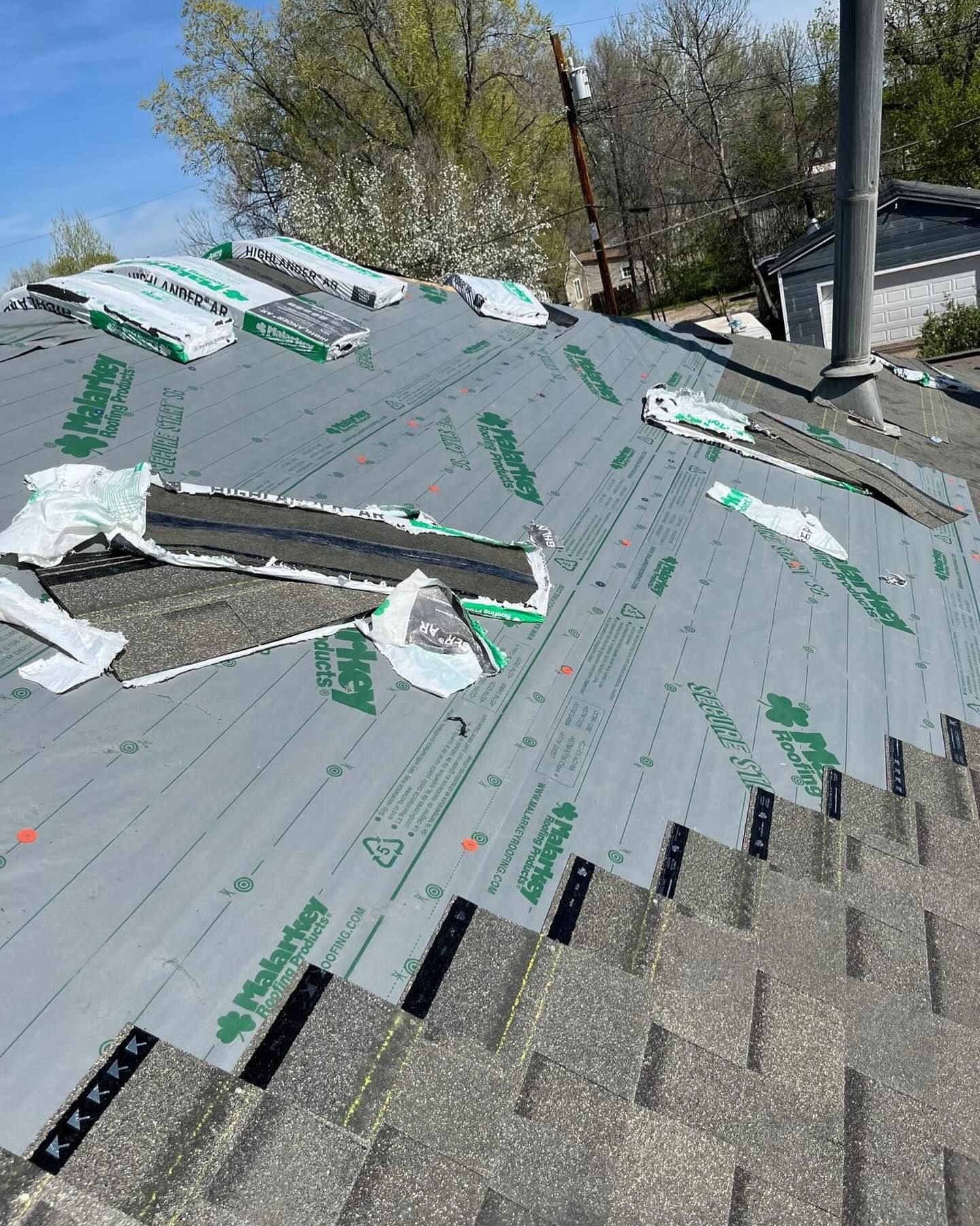 Roof under repair with gray underlayment, exposed shingles, and roofing materials