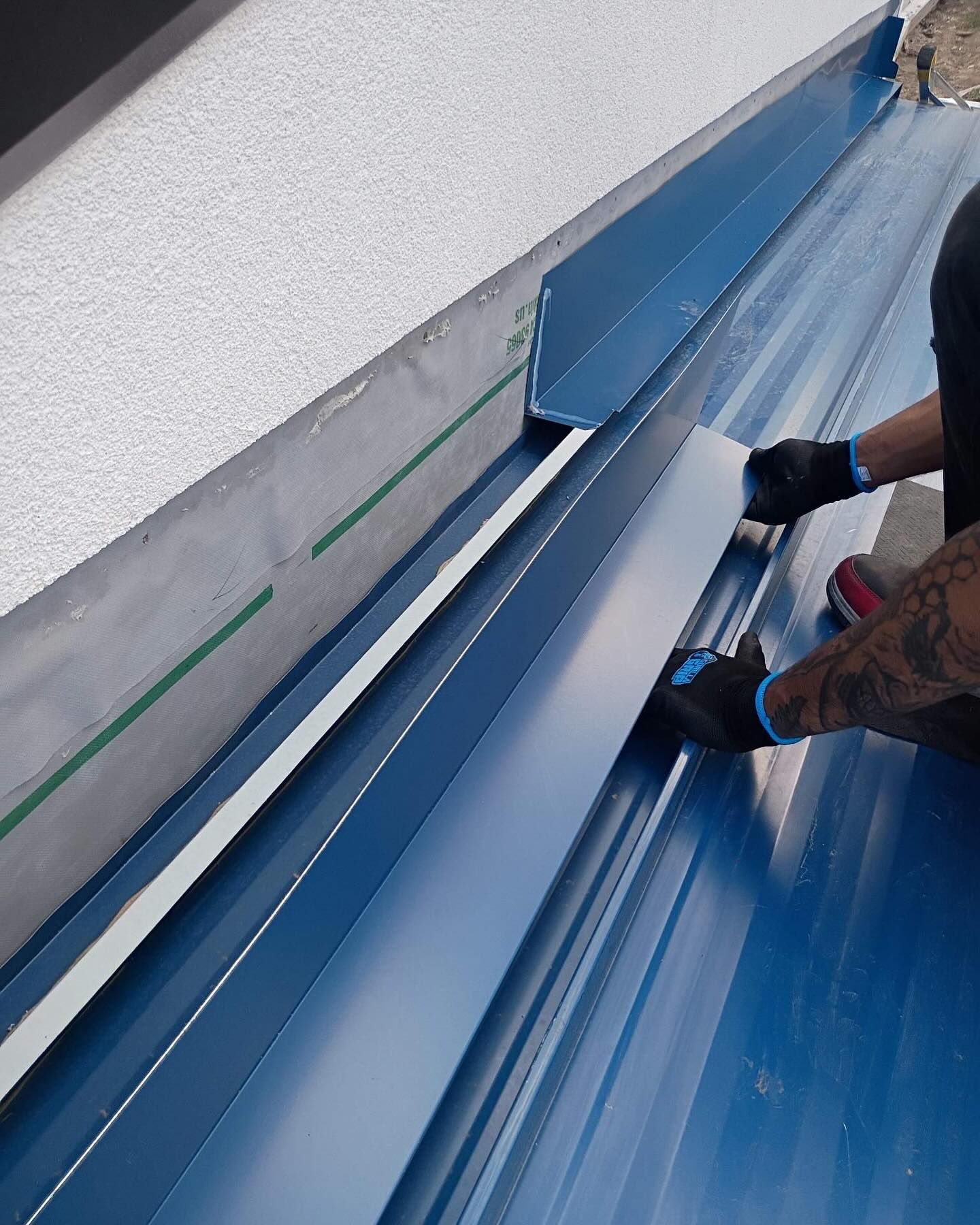 Worker installing blue metal roofing panels along a wall