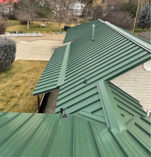Green metal roof on a house, viewed from above with a yard and driveway in the background.
